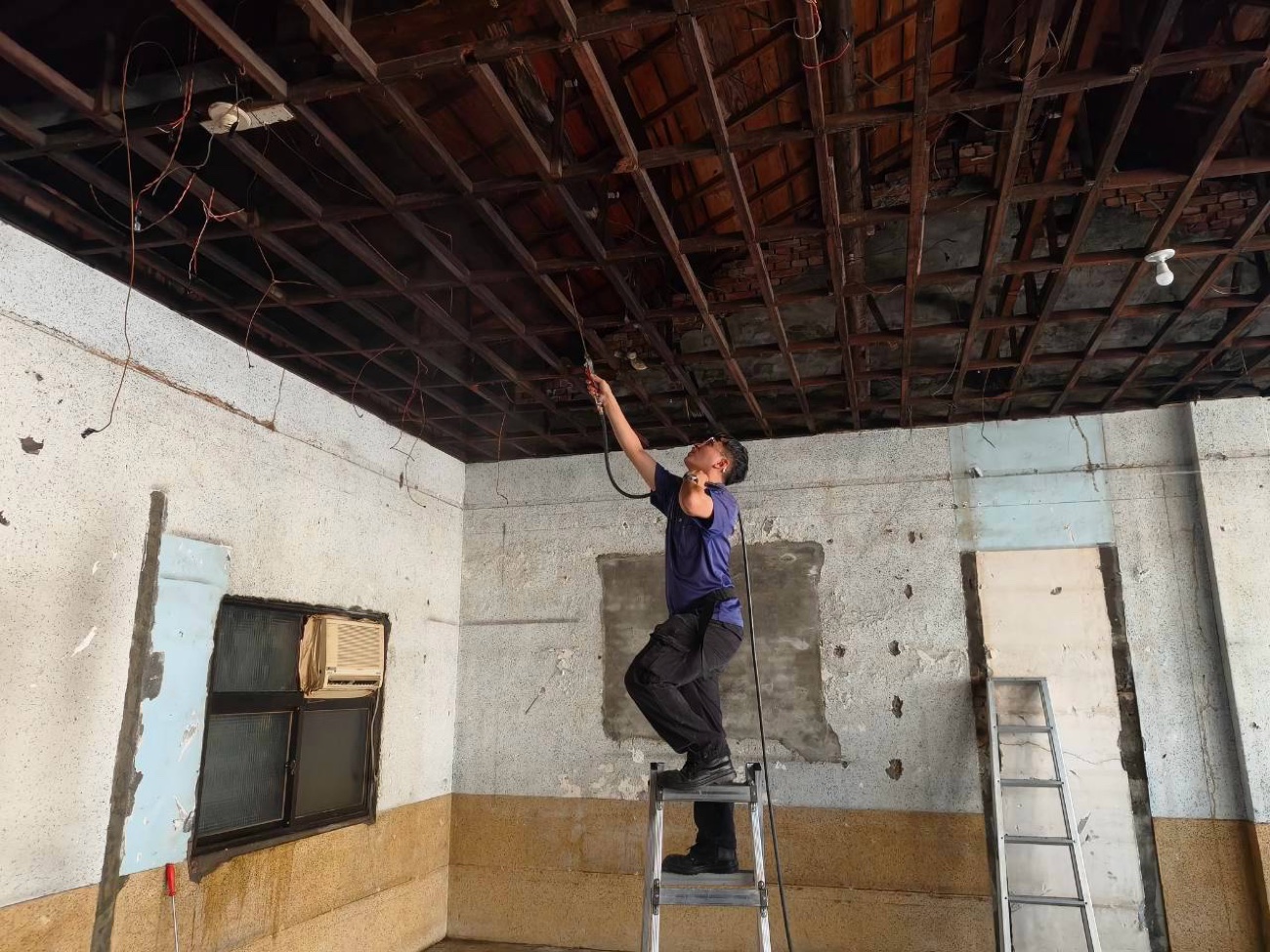 站上鋁梯對木造屋頂噴灑藥劑